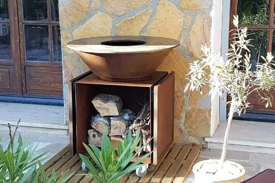 brasero artisanal en acier effet rouille pour barbecue avec rangement pour buche de bois et plan de travail pliable